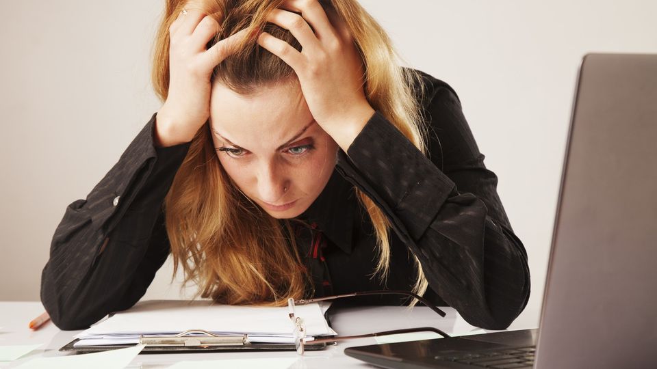 Eine Mitarbeiterin sitzt am Schreibtisch und ist mit ihrem Job unzufrieden. Sie rauft sich die Haare und starrt auf die Tischplatte.